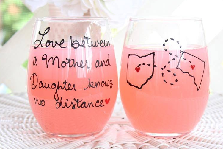 Two pink stemless wine glasses with engraved text on a white surface with flowers in the background.