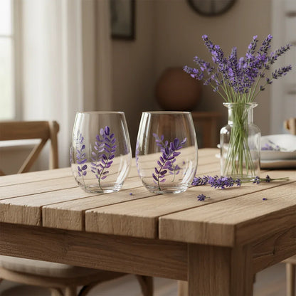 Two clear glasses with lavender designs on a wooden table, accompanied by a vase of lavender.