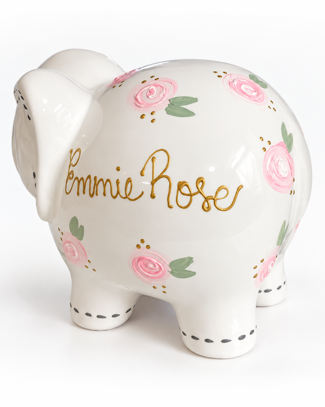 A white ceramic piggy bank shaped like an elephant, decorated with pink roses, green leaves, gold foil script reading 'Emmie Rose', and small gold dots, shown on a white background.