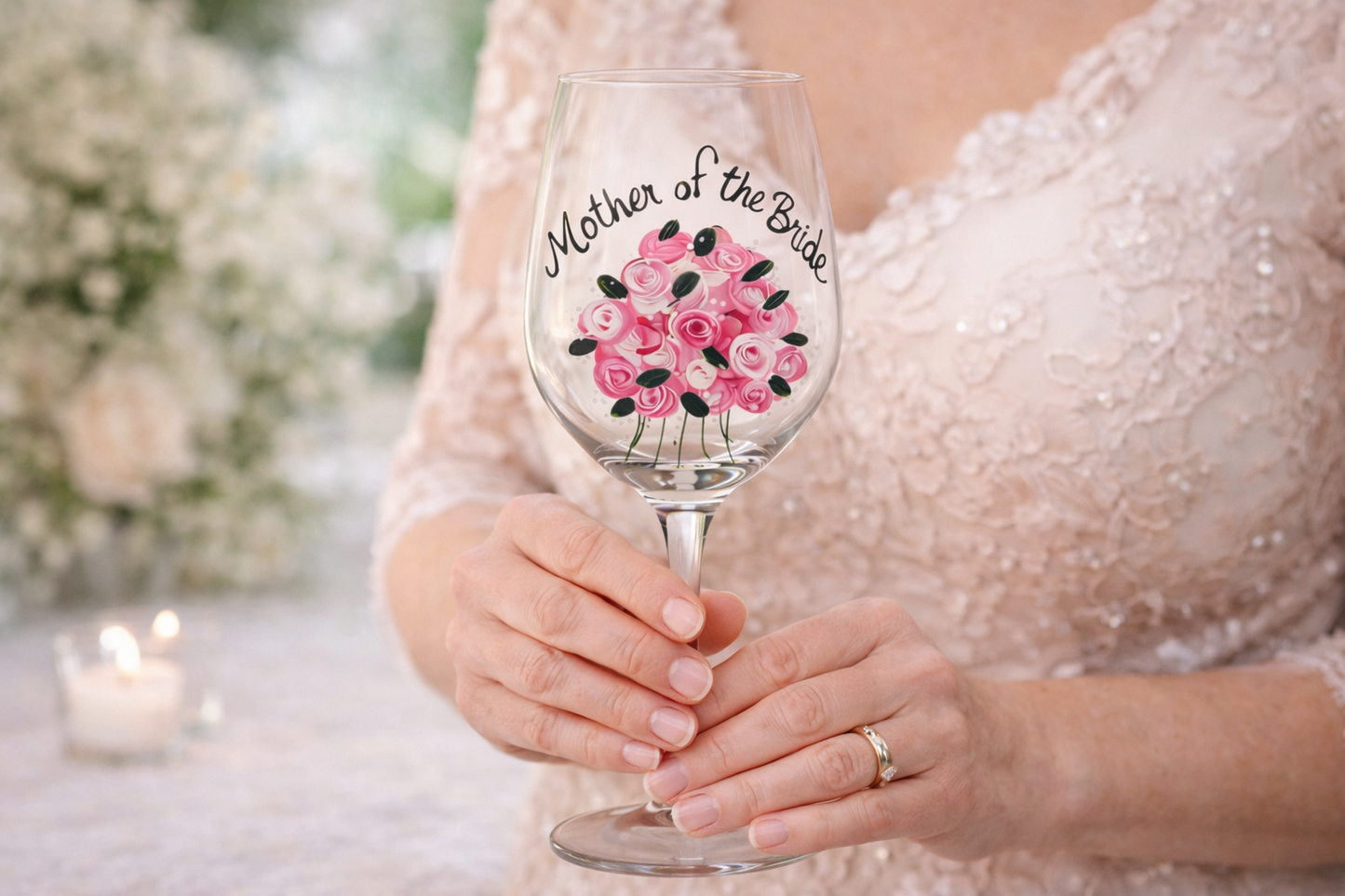 Wine glass with 'Mother of the Bride' text and floral design held by a person in a wedding dress.